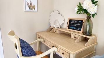 Un escritorio de madera con un marco que muestra una imagen de llamas, un espejo decorativo, un florero con flores blancas y una pizarra con normas de la casa.