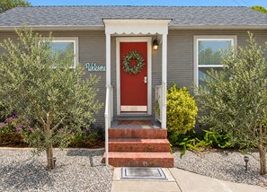A house with a red door, a welcome sign, and a wreath on the door. - Spacious Alameda Cottage with Private Garden (Alameda)