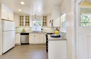 A kitchen with white cabinets, a dishwasher, a sink, and a window with a view of greenery.