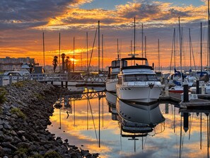 A marina with boats docked, a rocky shoreline, and a sunset in the background.