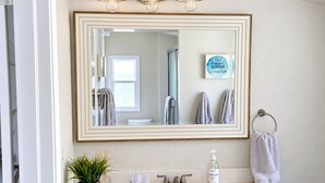 A bathroom with a large mirror, a sink, a towel rack, a hand soap dispenser, and a potted plant. - Spacious Alameda Cottage with Private Garden (Alameda)