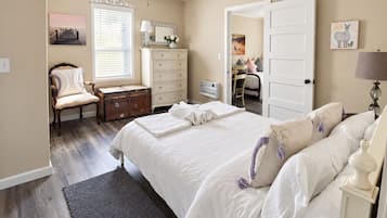 Ein Schlafzimmer mit einem großen Bett, einem Schminktisch, einem Sessel, einem Schreibtisch und einem Deckenventilator.