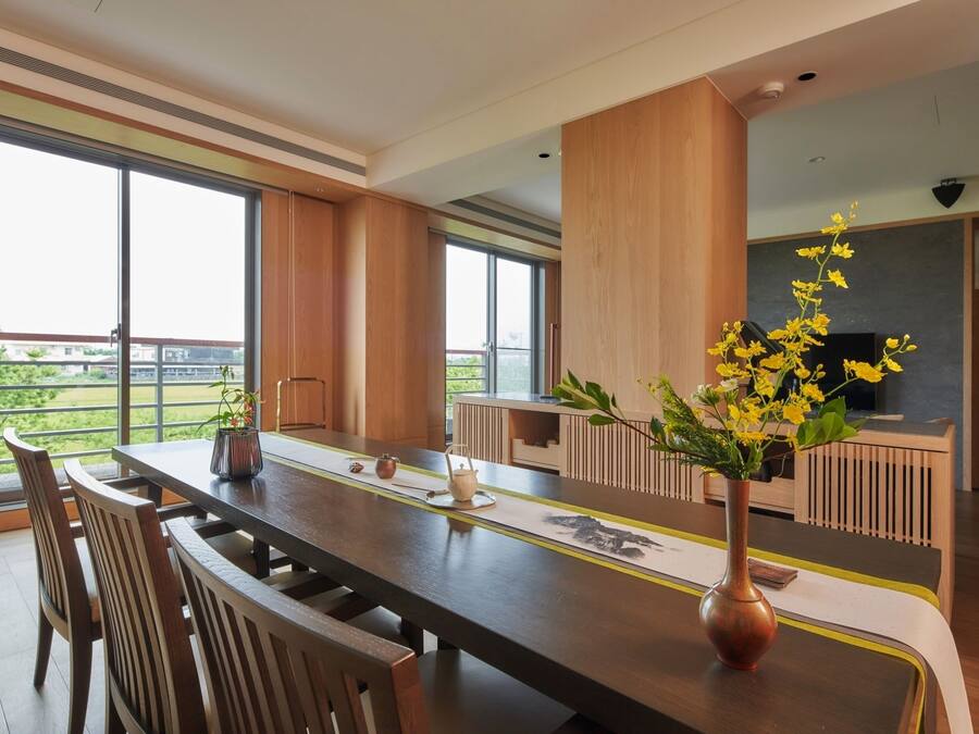 A modern dining area with a long table, chairs, and a vase of yellow flowers.