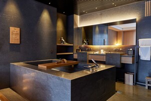 Un baño moderno con un lavamanos grande en el centro, un espejo encima y un estante de madera con una toalla.