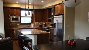 A modern kitchen with wooden cabinets, stainless steel appliances, and a large island with bar stools. - Luxury Condo, Private Hot Tub, Perfectly Located (Frisco)