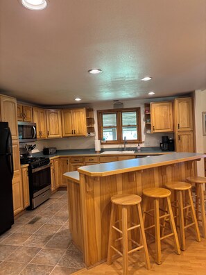 A kitchen with wooden cabinets, a stainless steel refrigerator, a microwave, a stove, and a large island with stools.