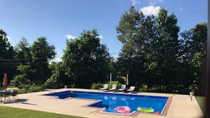 Una piscina rettangolare con bordo piastrellato, circondata da un prato e alberi.