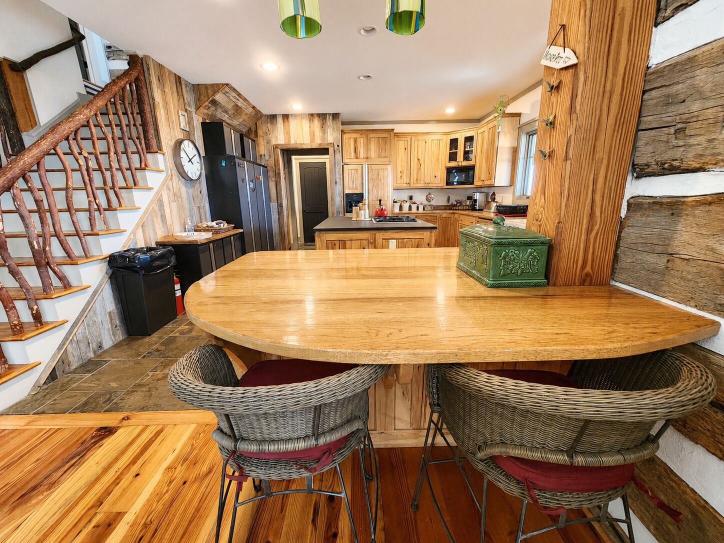 A kitchen with wooden cabinets, a round dining table, wicker chairs, and a staircase with wooden railings.