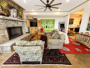 A living room with a stone fireplace, a ceiling fan, a green cabinet, and a red rug.