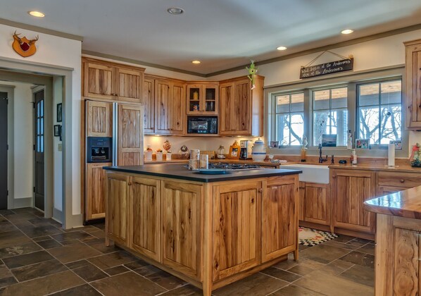 A spacious kitchen with wooden cabinets, a large island, and a view of the outdoors through large windows.