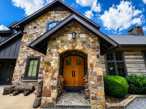 A stone house with a wooden front door, a stone chimney, and a log stack outside.