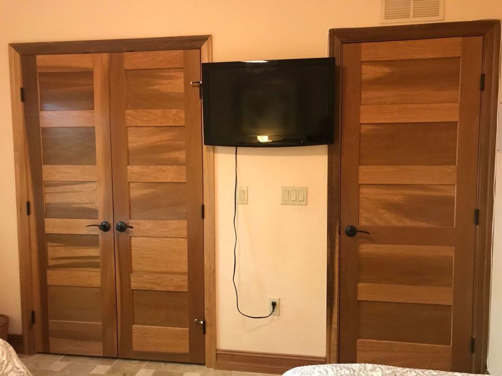 A room with two wooden doors, a television mounted on the wall, and a power outlet.