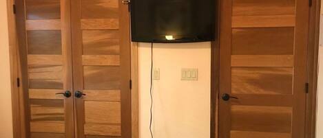 A room with two wooden doors, a television mounted on the wall, and a power outlet.