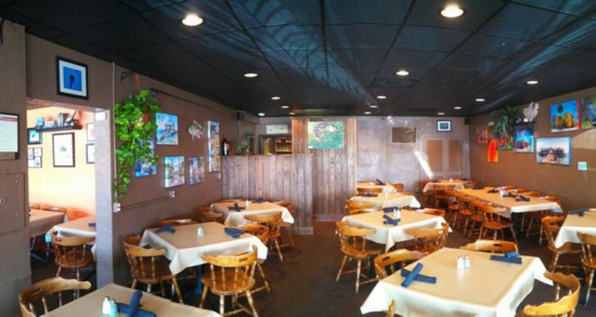 A restaurant with multiple tables and chairs, wooden walls, and framed pictures on the walls.