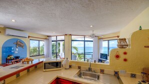 A kitchen with a large window, a microwave, a sink, and a ceiling fan. - Penthouse view of the Caribbean with AC, WiFi, easy beach access! (Akumal)