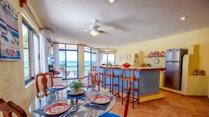A spacious kitchen with a large island, a dining area with a glass table, and a view of the ocean. - Penthouse view of the Caribbean with AC, WiFi, easy beach access! (Akumal)