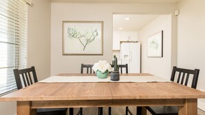 Une salle à manger avec une table en bois, des chaises noires et des œuvres d’art encadrées accrochées aux murs.