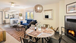 A modern living room with a fireplace, a dining area with a round table, and a kitchen in the background. - Outpost: Pitchfork 446 - Close to Snow King Mtn! (Jackson)