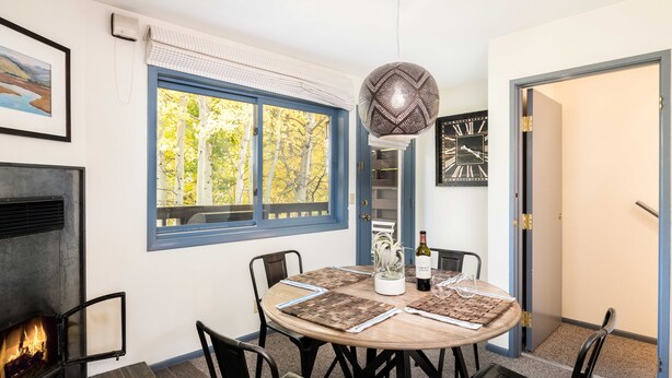A dining area with a round table, chairs, a fireplace, and a view of trees through a window. - Outpost: Pitchfork 446 - Close to Snow King Mtn! (Jackson)