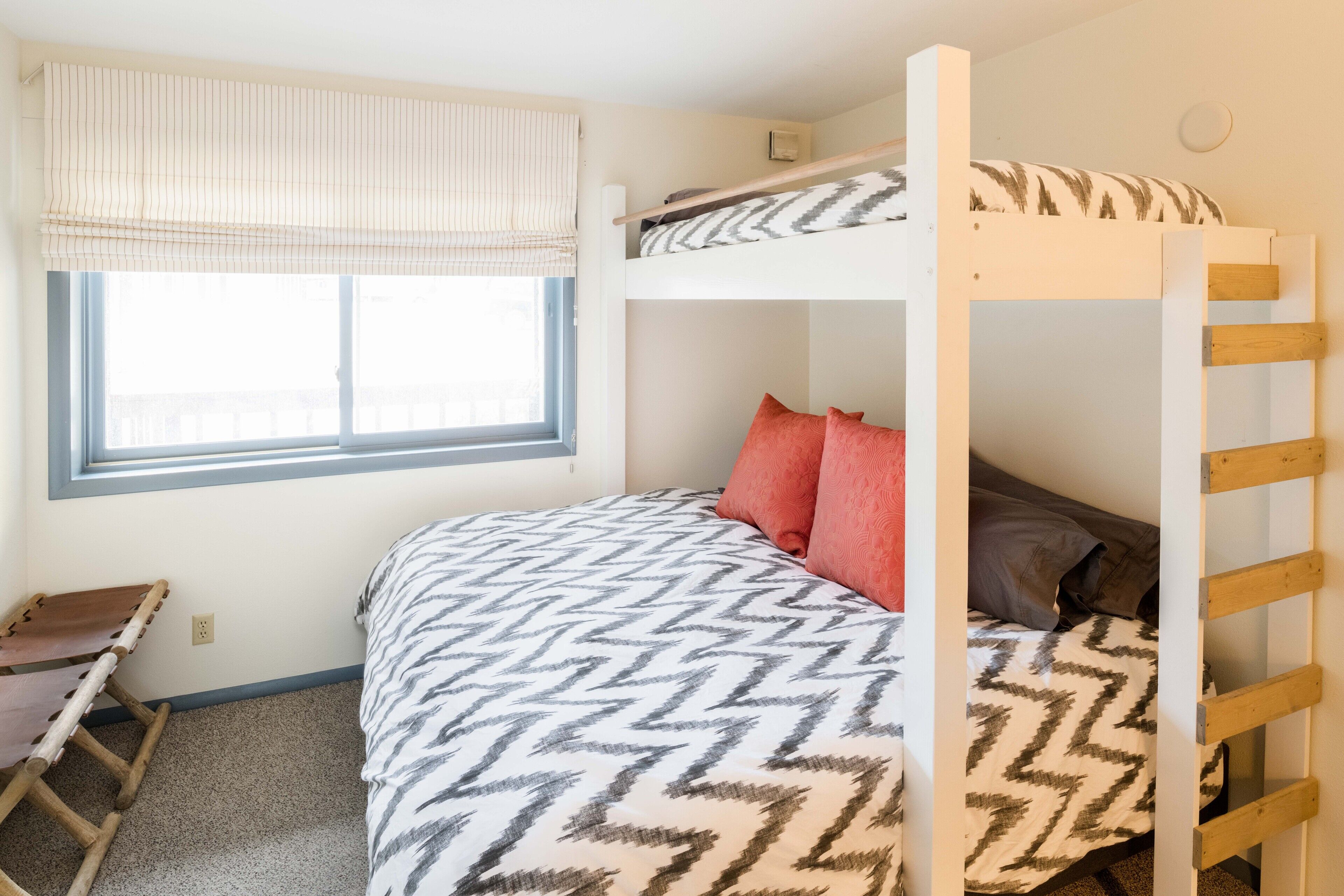 A bunk bed room with a window, a desk, and a chair.