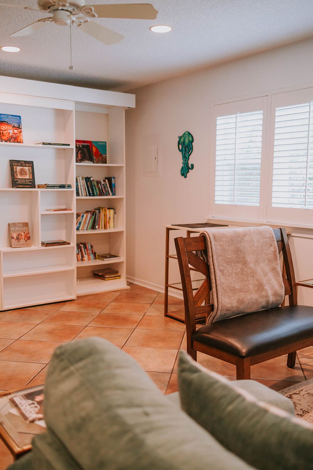 Una sala de estar con una estantería, un sillón y una ventana con persianas.