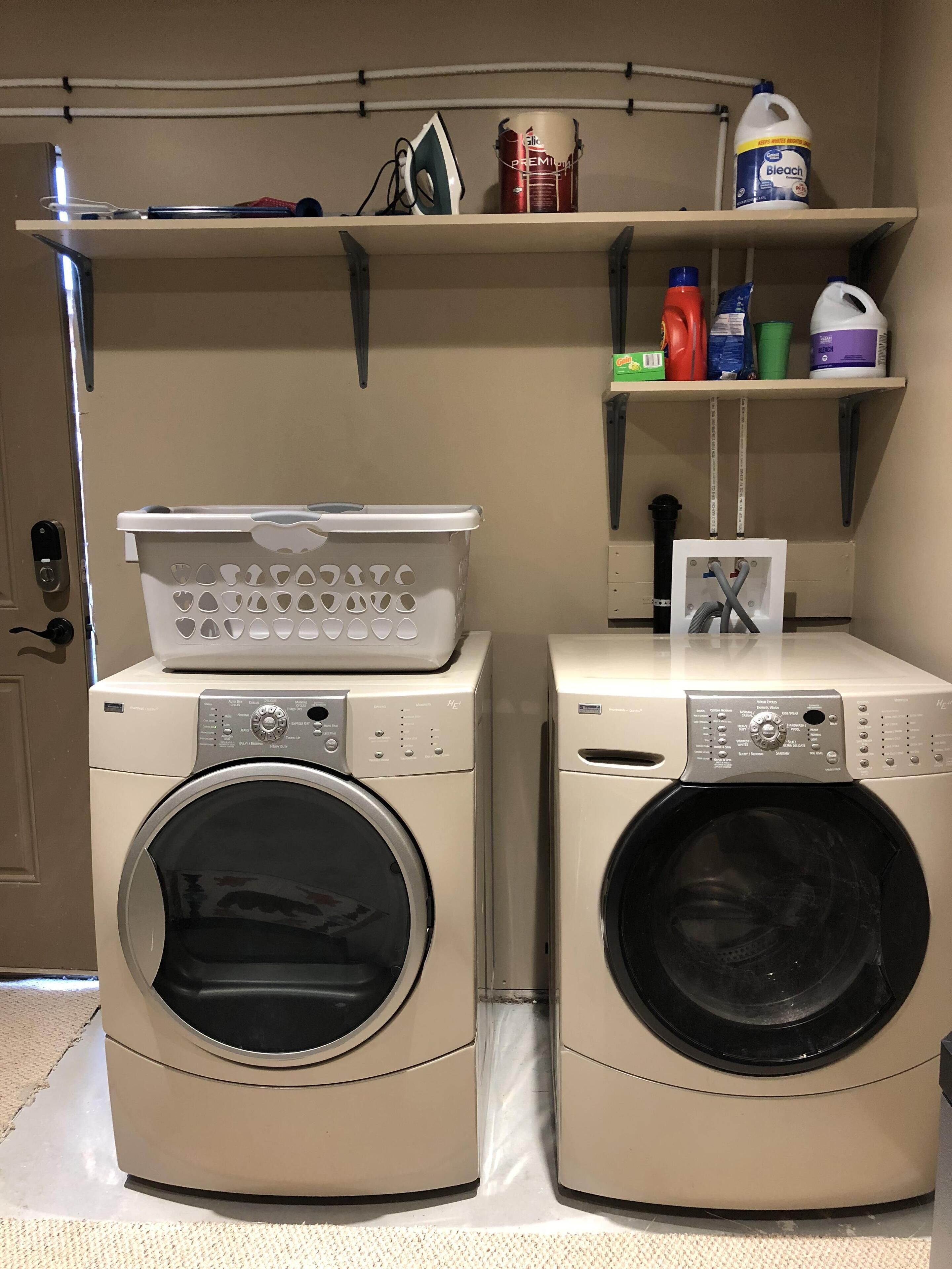 Two front-loading washing machines, a laundry basket, and shelves with cleaning supplies.