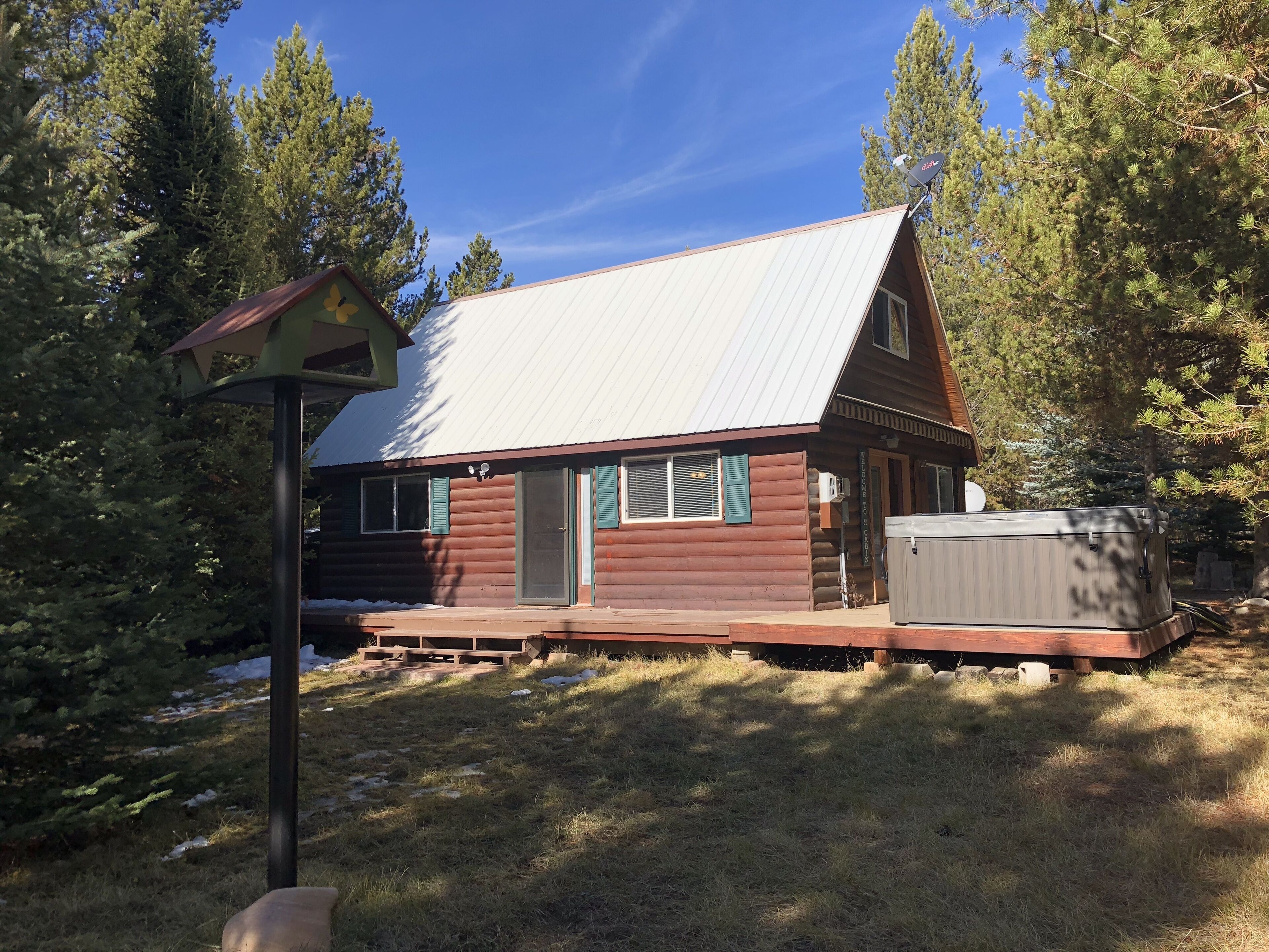A cabin with a metal roof, a deck, and a hot tub.
