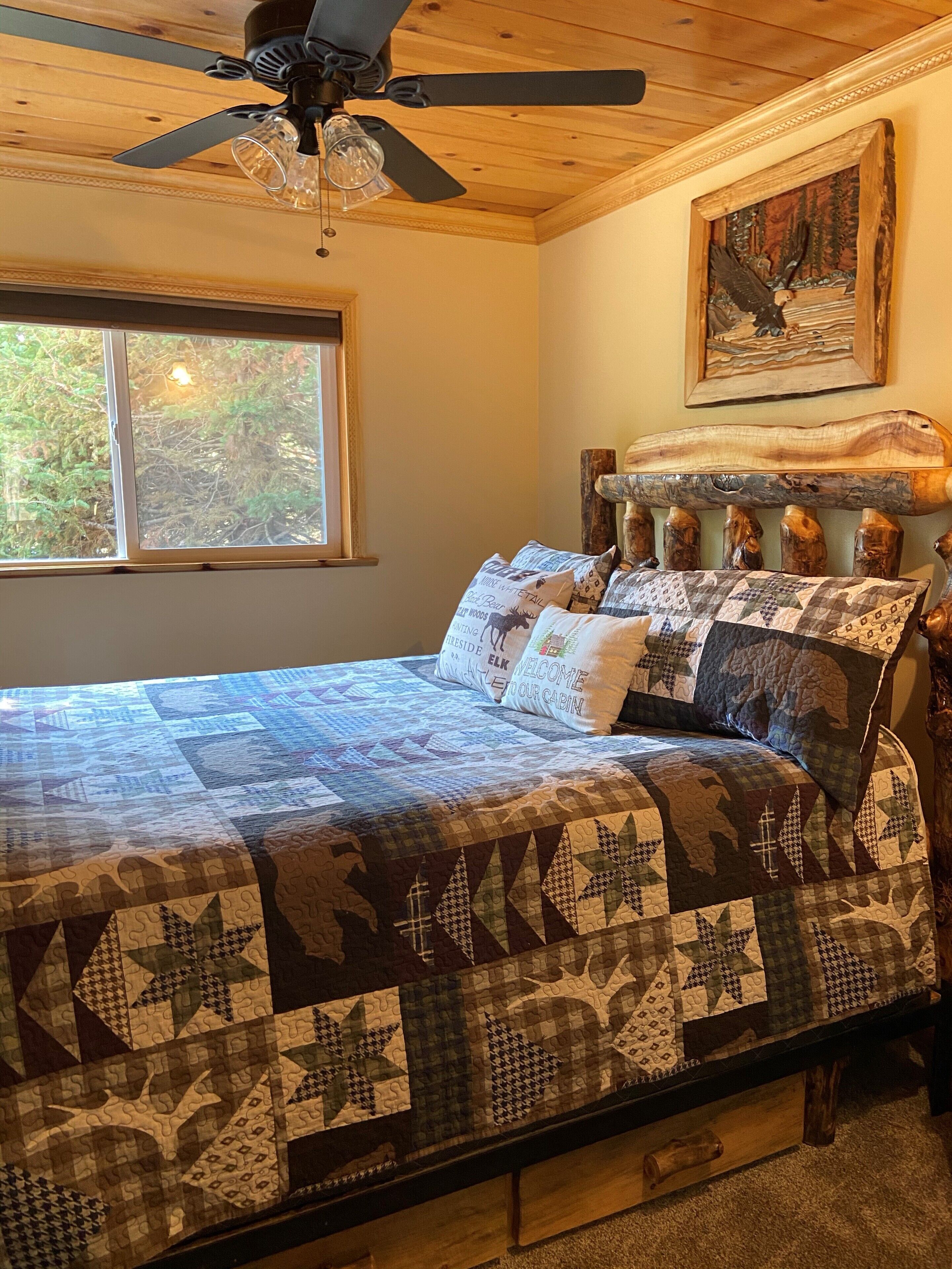 A bedroom with a wooden headboard, a quilted bedspread, and a window with a view of trees.