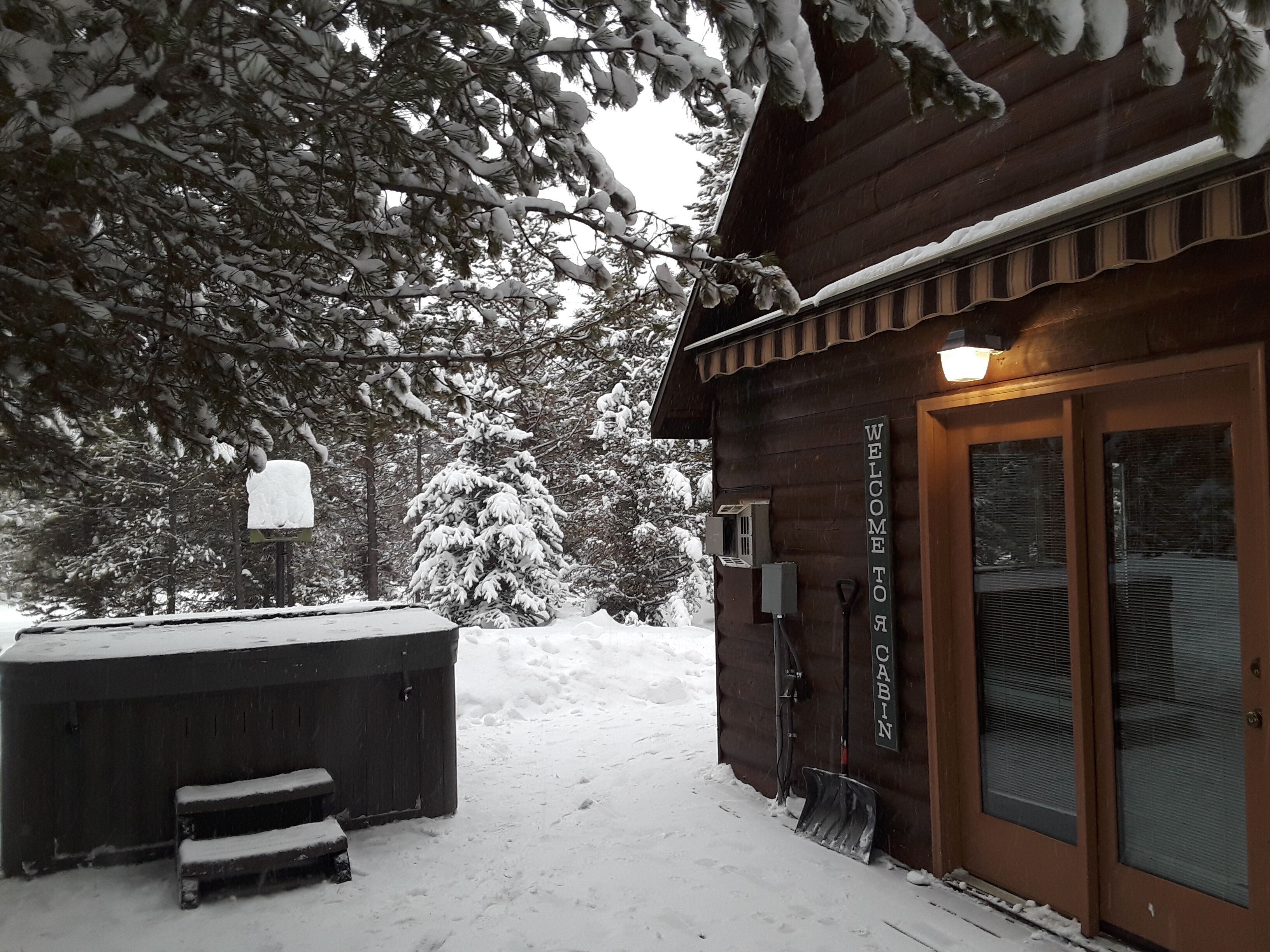 A wooden cabin with a 'Welcome to Cabin' sign, a hot tub, and a snow-covered landscape.