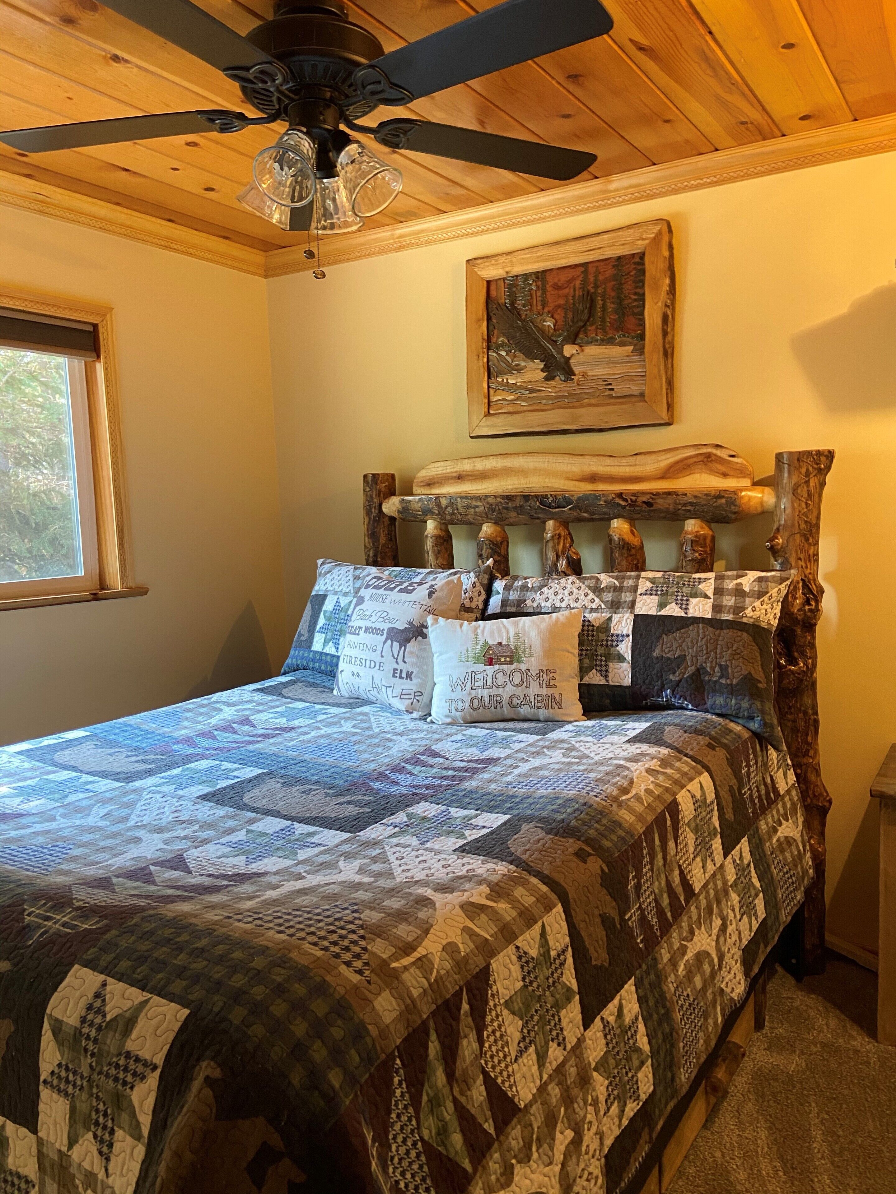 A bedroom with a wooden headboard, a quilted bedspread, and a ceiling fan.