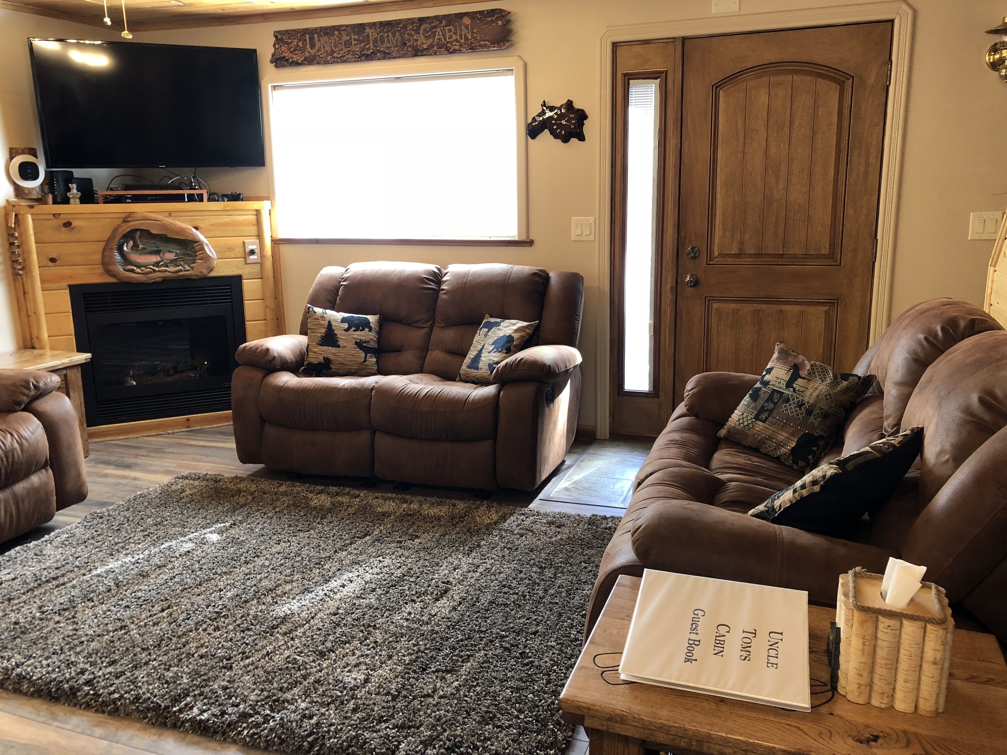 Una sala de estar con chimenea, sofás de cuero, un televisor de pantalla plana y una puerta de madera.