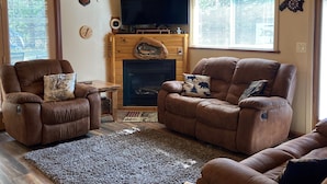 A cozy living room with a fireplace, leather sofas, a wooden ceiling, and a large TV. - Woodland retreat/hot tub/Near Yellowstone (island park)