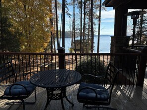 A wooden deck with a round table and two chairs, overlooking a lake with trees in the background. - Main Lake Log Home Retreat - pizza oven, fire pit, kayaks, SUP, pontoon (Henrico)