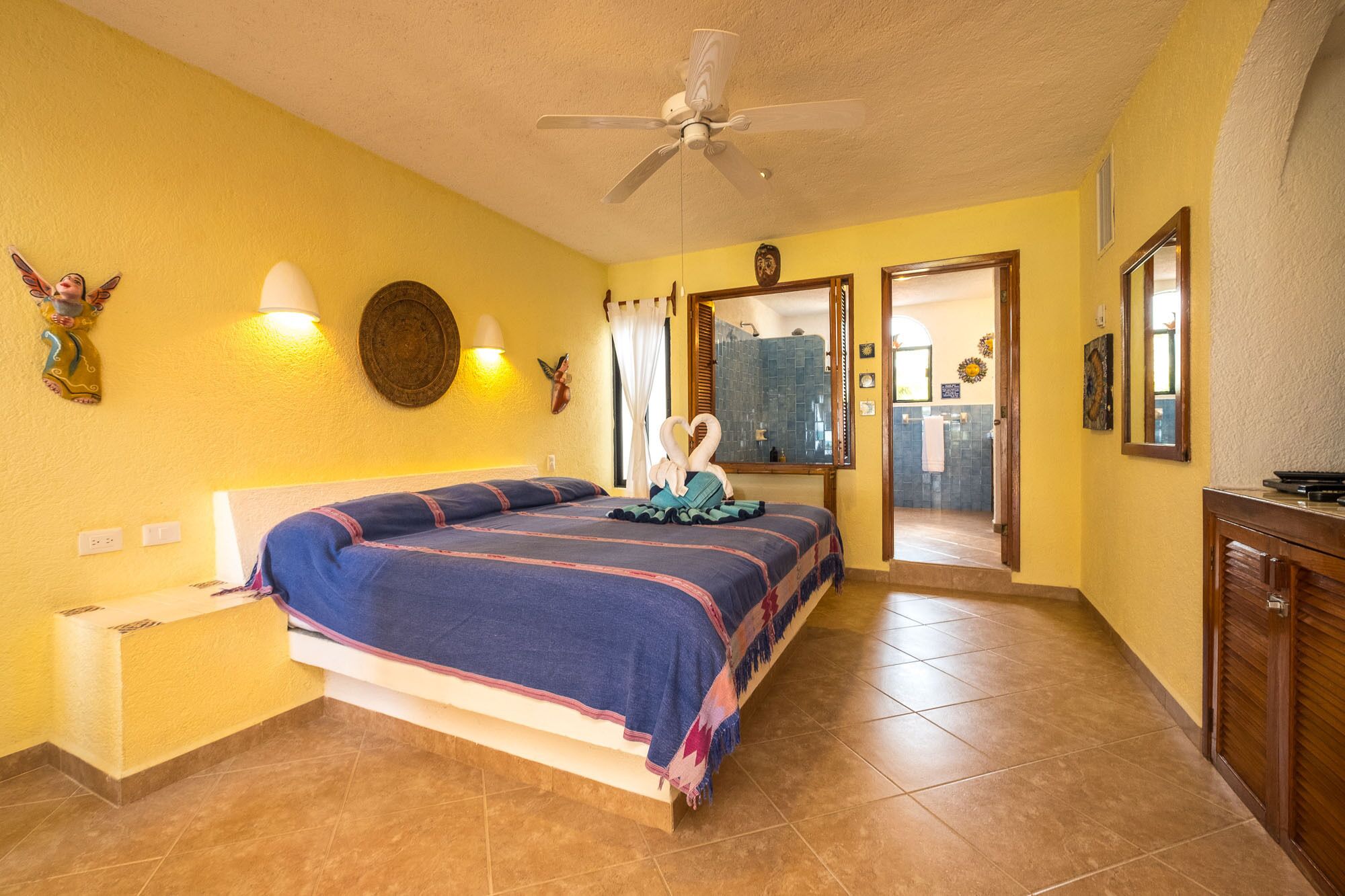 A hotel room with a bed, a ceiling fan, a bathroom visible through an open door, and a wooden dresser.