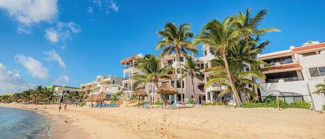 A beachside hotel with multiple floors, palm trees, and beach chairs.