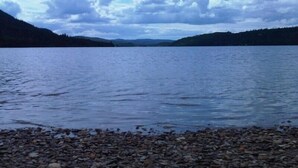 Un llac amb riba de pedres i muntanyes allunyades sota un cel nuvolós.