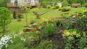 Una casa amb terrassa, envoltada d'un jardí ben cuidat i ple de plantes i flors.