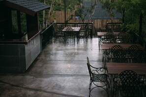 An outdoor patio area with tables and chairs, a wooden fence, and a building with a sloped roof. - Forest Pool Villas (Pattaya)