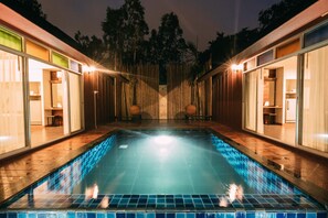 A swimming pool with a tiled edge, surrounded by wooden walls and glass doors, with lights along the perimeter. - Forest Pool Villas (Pattaya)