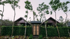 Une maison traditionnelle en bois, dotée d’une entrée centrale et entourée d’une végétation luxuriante et de parterres de fleurs aux couleurs vives.