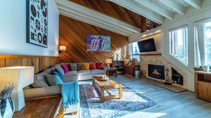 A spacious living room with a wooden ceiling, a fireplace, a large TV, and a cozy seating area. - Walk to Ski Condo + Views, Fireplace, Jacuzzi 438 (Mammoth Lakes)