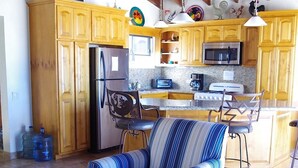 A spacious kitchen with wooden cabinets, a refrigerator, a microwave, and a stove. There is a striped armchair and a wooden table with a tray. - Casa Bianchi Private Beach View Home Las Conchas (Puerto Peñasco)