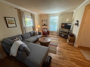 A living room with a sofa, a coffee table, a TV, and a lamp. - Locust Street Cottage | Charming Walla Walla Stay (Walla Walla)