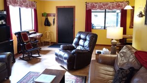 Ein Wohnzimmer mit einem braunen Ledersofa, einem Holzschaukelstuhl, einem schwarzen Ledersessel und einem beigen Sofa. Im Raum befindet sich ein Couchtisch und ein Teppich mit Muster.