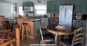 Une cuisine avec des armoires de couleur turquoise, un réfrigérateur blanc, des chaises en bois et une table à manger.