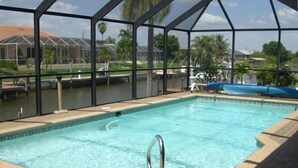 A swimming pool with a clear blue water, surrounded by a covered area with a metal frame and a tiled floor.