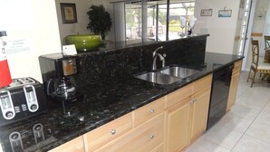 A kitchen with a black granite countertop, stainless steel sink, wooden cabinets, and a coffee maker.
