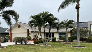 A residential house with a well-maintained lawn, palm trees, and a garage.