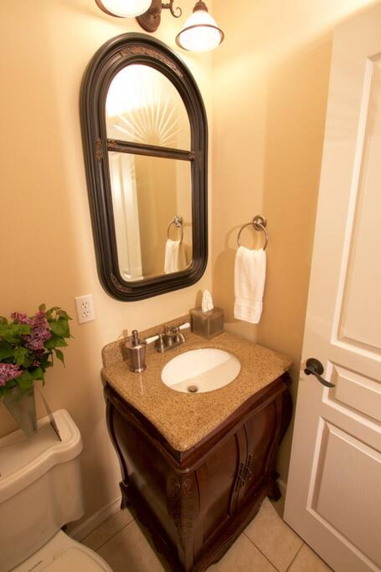 Un baño con tocador, lavabo, espejo, perchero para toallas y una planta en maceta.