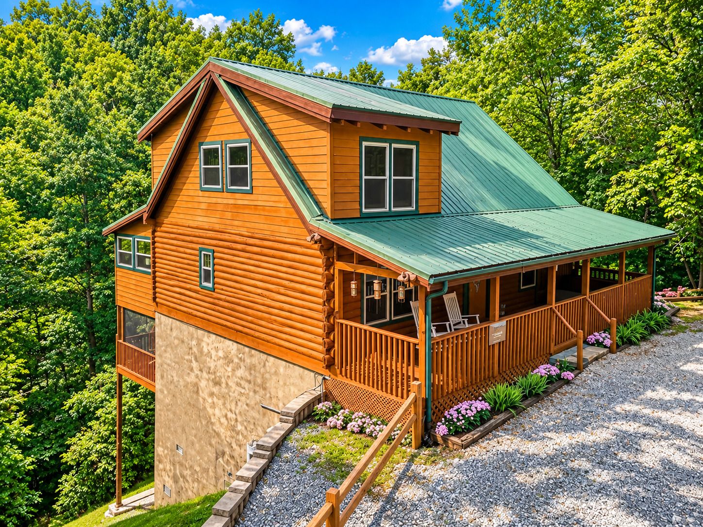 A log cabin with a green roof, a porch with outdoor seating, and a gravel driveway.